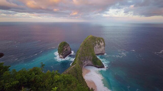 Epic Coastal View of Kelingking Beach With Towering Limestone Cliffs Turquoise Ocean and Dramatic Cloudy Sky in Slow Motion