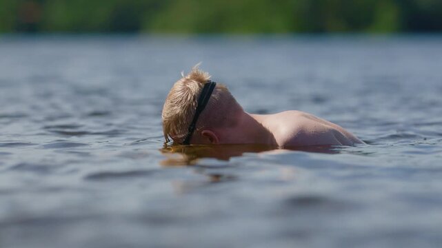 Blond swimmer with goggles floating peacefully in sunny lake water