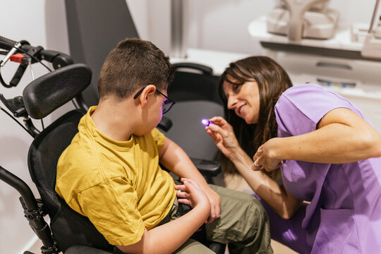 Optometrist using penlight examining little boy with cerebral palsy in wheelchair