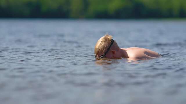 Young swimmer wearing goggles relaxing face down in calm lake water