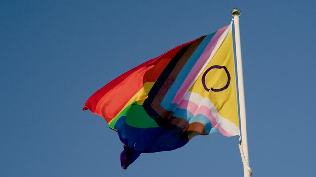 Progress pride rainbow flag waving brightly against clear blue sky