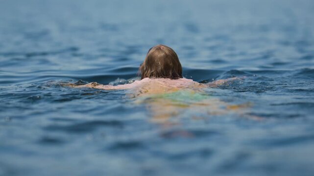 Child swimming away through rippling blue lake water in summer