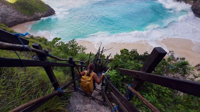 Female Backpacker Slowly Making Her Way Down the Hazardous Staircase to Kelingking Beach Above Powerful Ocean Waves in Slow Motion