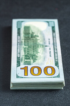 Stack of one hundred dollar bills sits on dark surface