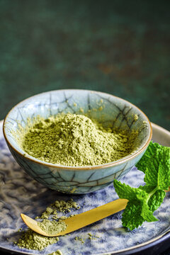 Ground matcha powder in ceramic bowl with spoon and mint leaves