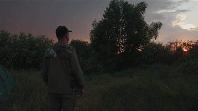 Young adult man hiker enjoys sunset and stormy dark sky with lightnings