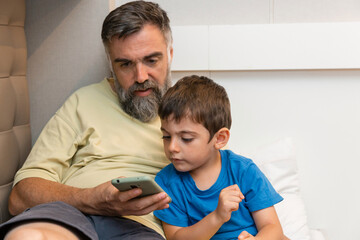 Fototapeta premium Father and son using smartphone in boat cabin