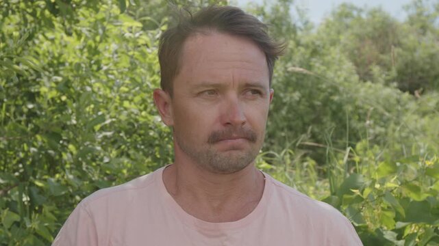 Medium shot portrait of the young adult caucasian man talking something on the camera with natural green background