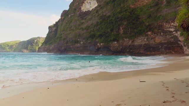 Gentle Surf and Turquoise Water Meeting the Sandy Shore of Kelingking Beach Beneath Dramatic Coastal Cliffs in Slow Motion