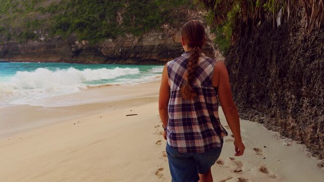 Female Traveler Walking Along the Sandy Shore of Kelingking Beach Beside Powerful Ocean Waves in Slow Motion