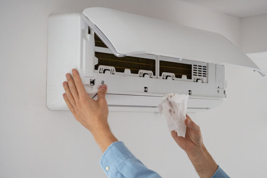Man's hands wiping inside parts of indoor air conditioner on wall with alcohol wipe to remove dust, male servicing home climate control cooling system, cleans dirt with tissue, appliance maintenance.