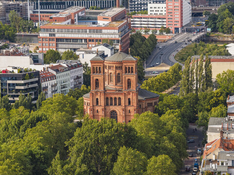 Aerial view of the historic red brick St. Thomas Church surrounded by lush green trees and urban architecture in Berlin, Berlin, Germany.