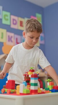 Boy stacking colorful blocks with his hands on a table amid alphabet cards in a school building; concentration creativity.
