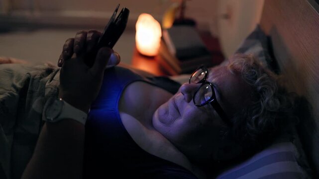 Overweight Happy Mature Female Browsing Social Media On Phone Lying In Bed At Night
