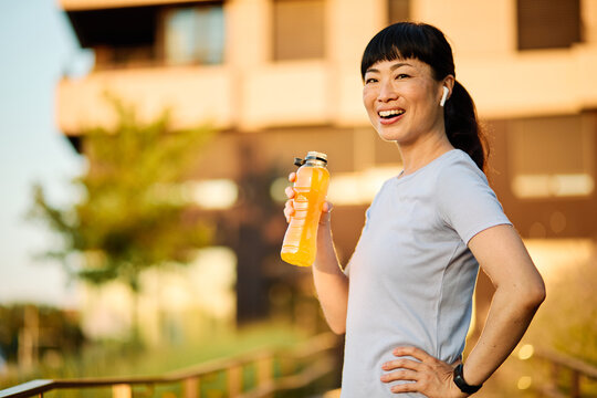 Portrait of a young beautiful sport woman smiling happy and confident. Standing and  doing exercise and stretching and holding a bottle of water or energy drink or juice during a break in city park ou