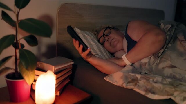 Overweight Exhausted Older Lady Falling Asleep Dropping Phone On Books At Night