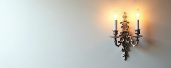 Obraz premium Antique silver wall sconce with two candle bulbs emits warm glow. Classic ornate design mounts on bright white wall. Adds elegance and vintage charm to interior spaces.