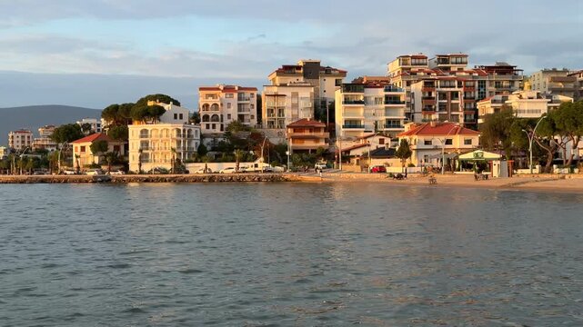 Scenic coastal view of Gulluk, Turkey, featuring white resort hotels and residential buildings along the waterfront, illuminated by the warm glow of late afternoon sun.