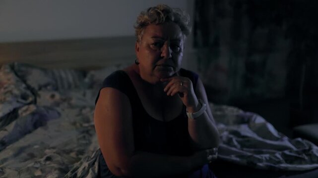 Overweight Pensive Senior Woman Resting Chin On Hand In Dark Bedroom At Night