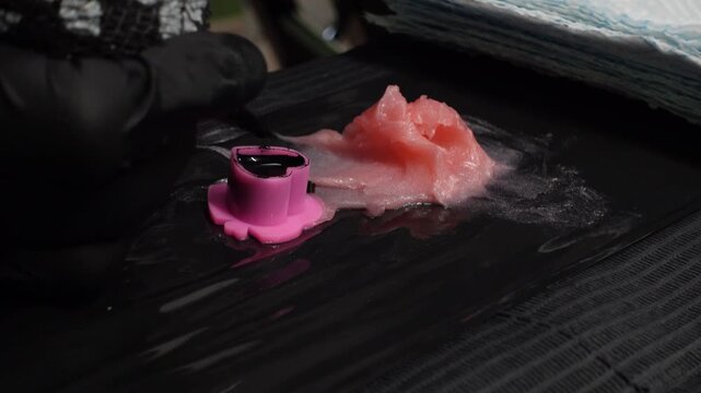 Close-up of a tattoo artist dipping a cartridge needle into a ink cap next to pink petroleum jelly during a tattoo session