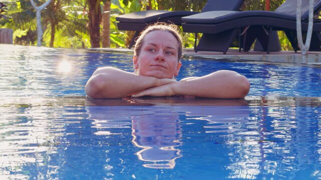 Young Woman Resting At Edge Of Blue Swimming Pool In Tropical Resort, Mindfulness And Peaceful Vacation