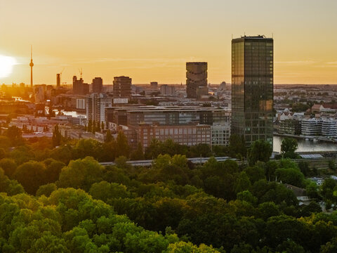 Aerial view of the Berlin skyline with the TV Tower and modern skyscrapers rising above lush green trees along the Spree river at golden hour in Berlin, Berlin, Germany.
