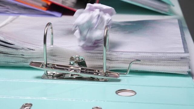 Crumpled paper resting on an open light blue ring binder filled with documents, symbolizing project failure, business stress, and wasted effort in an office environment