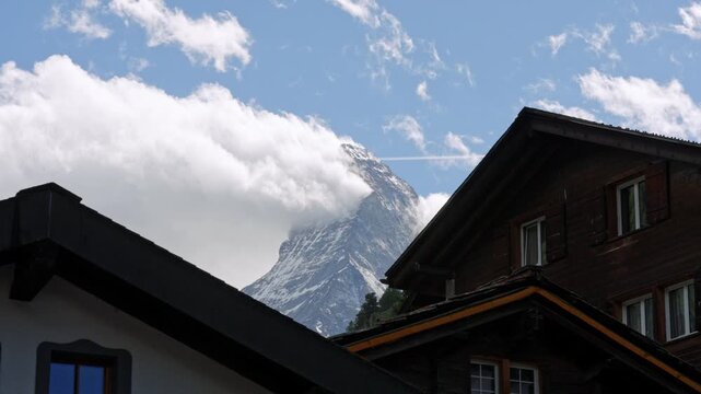 Majestic matterhorn mountain peak appearing from clouds above traditional swiss chalet roofs