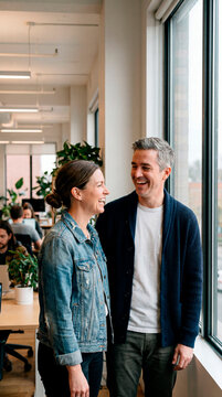 Two colleagues laughing together by window in bright modern startup office space