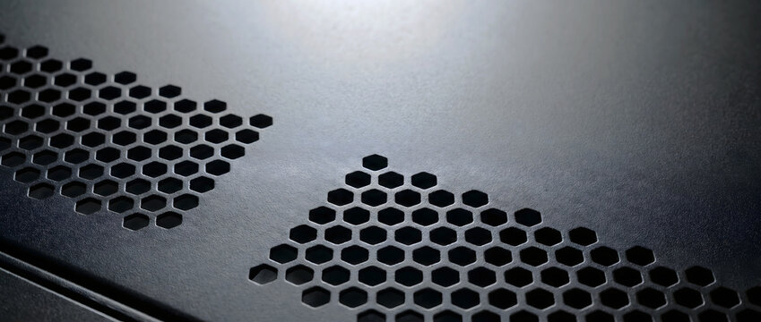 Close-up of black metal surface with hexagonal ventilation holes for digital infrastructure equipment