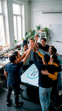 Diverse startup team celebrating project success around interactive touchscreen display