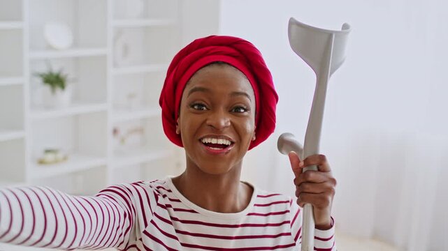 Smiling African American Woman With Crutches Taking A Selfie In Cozy Living Room, Expressing Positivity And Joy While Utilizing Mobility Aid, Celebrating Resilience At Home, Healthcare Concept.