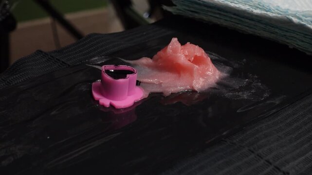 Close-up of a tattoo artist dipping a cartridge needle into a ink cap next to pink petroleum jelly during a tattoo session