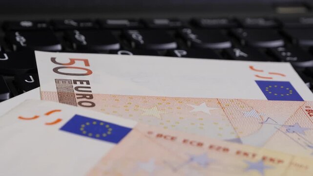 Close-up view of euro banknotes placed on a laptop keyboard, highlighting the denominations and design elements of the currency, with the keyboard's keys visible in the background