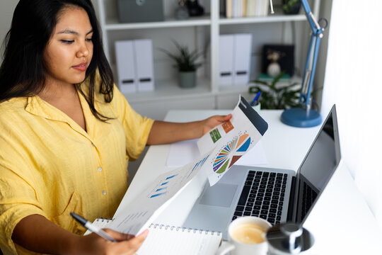 Focused latina accountant analyzing charts and reports in modern office