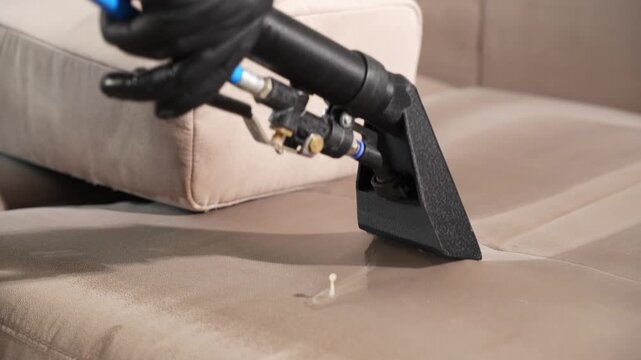 Upholstery dirt extraction using a vacuum nozzle on a beige sofa captured in 4K. Cleaning worker removes stains and liquid from fabric furniture