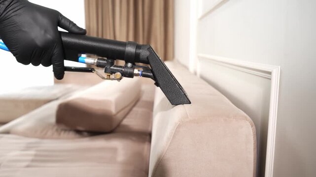 Fabric sofa deep washing procedure utilizing a commercial extraction machine in 4K. Janitorial worker in black gloves vacuums chemical detergent from upholstery