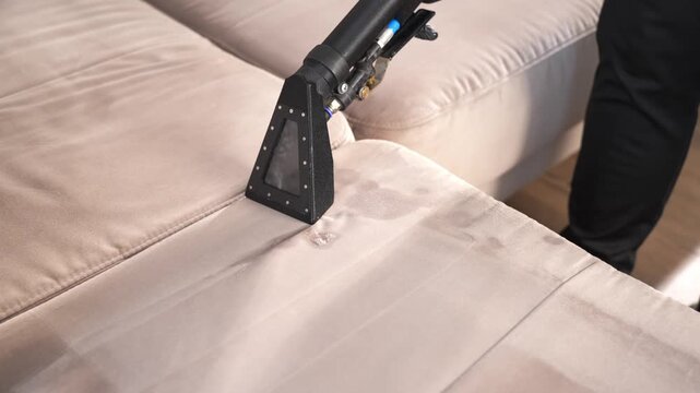 Upholstery water recovery process using an electric extractor machine in 4K. Cleaning staff removes moisture from a beige residential sofa