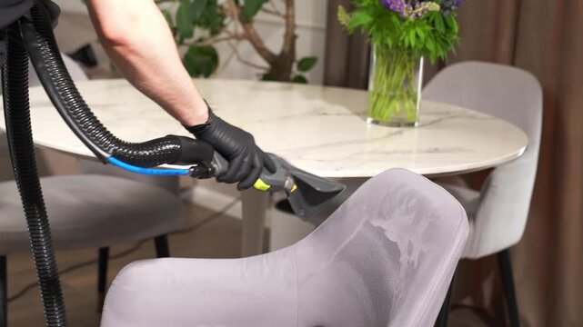 Deep dirt suction on an upholstered dining chair recorded in 4K. Worker uses a wet vacuum tool to remove stains from textile