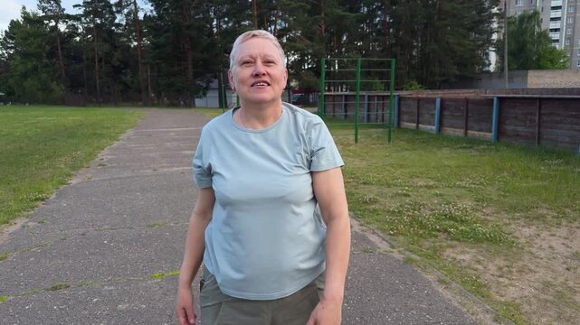 A mature woman does arm exercises on an outdoor sports ground at a stadium, active fitness for seniors and a healthy lifestyle