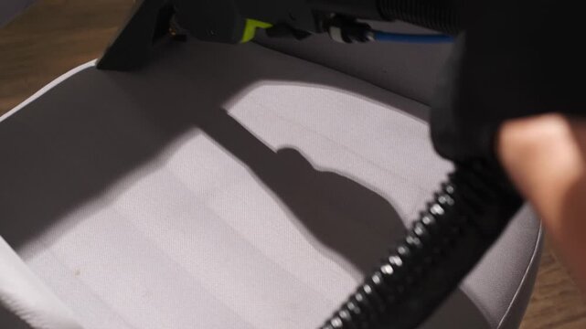 Chair cushion moisture suction using industrial equipment in 4K. Worker performs deep extraction on a gray upholstered surface