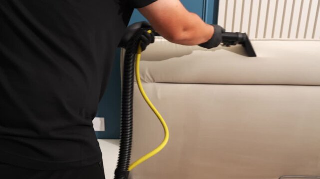 Textile sofa headrest sanitization using a wet vacuum tool shot in 4K. Worker removes cleaning detergent and soil from the upholstery