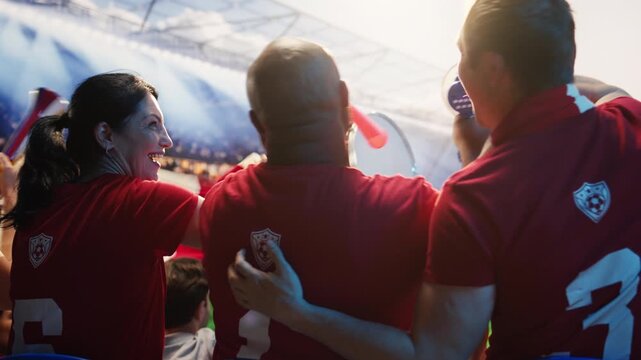 Supporters in red soccer kits blowing vuvuzelas during match day in packed stadium, showing cheering crowd creates passionate fan chants with air horns to show team support for fan culture content.