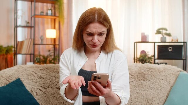 Middle-aged woman scrolls comments on smartphone at home, frowning and waving her hand with frustration stress. Young adult girl shows nervous reaction to negative feedback, visibly annoyed and tense.