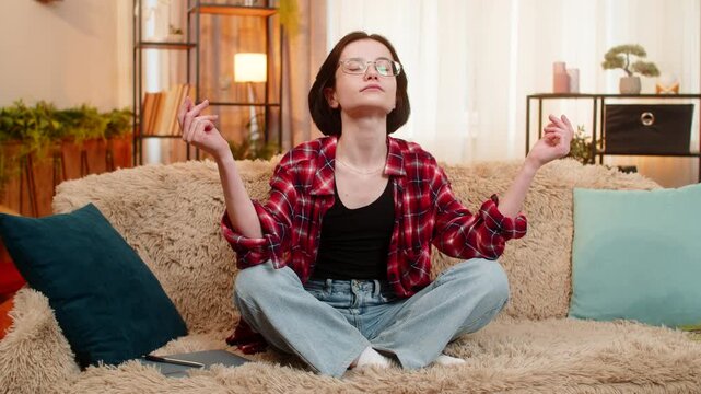 Young woman writes in personal journal after meditation while sitting on home sofa, looking thoughtful and calm. Girl feels peaceful and balanced, reflecting on inner clarity and emotional stillness.