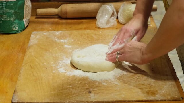 Chef shaping soft pizza dough by hand on a floured wooden table before baking. Traditional homemade pizza preparation using fresh ingredients in a rustic kitchen environment