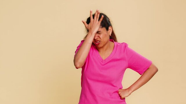 Indian woman theatrically places hand on forehead dramatically performing facepalm over foolishness. Girl on beige background humorously expressing frustration disbelief funny reaction silly mistake