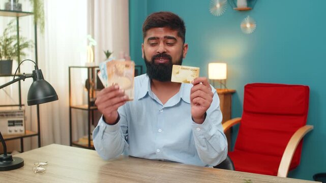 Indian man at home shows credit card with euro cash promoting withdrawal loan option displays money power. Arabian guy offers funds waving banknotes encouraging secure payment gain credit benefit