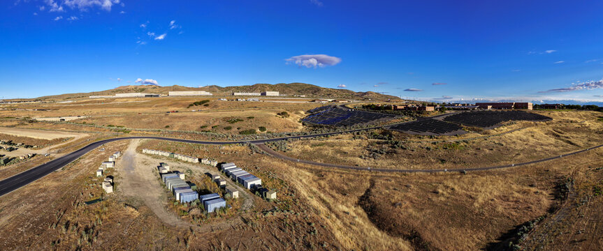 Aerial panorama of the Utah Data Center, Camp Williams Army Base, and a solar panel field set against the arid landscape of Bluffdale, Utah, United States.