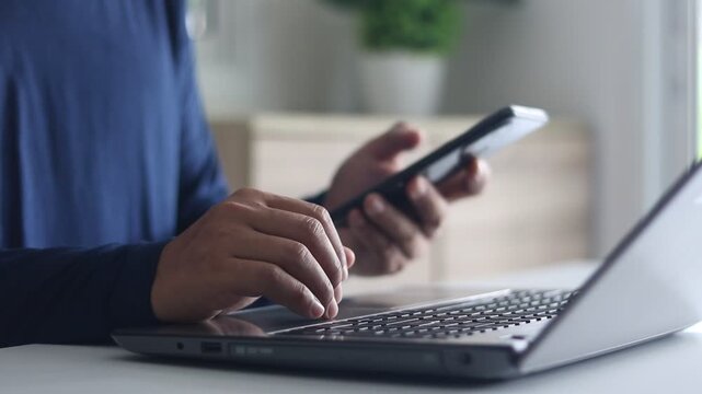 Close-up of a man's hands typing a password on a laptop keyboard and using a smartphone for two-factor authentication, ensuring data security and online privacy. Cybersecurity concept.